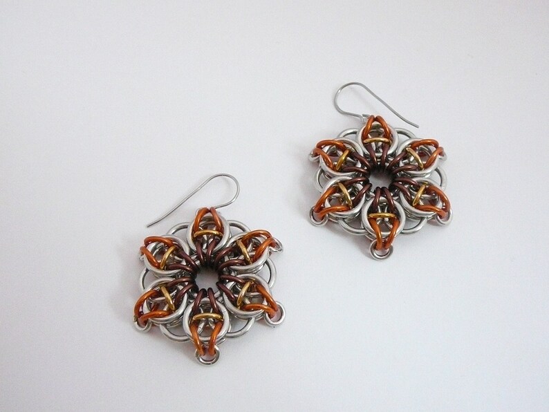 May include: A pair of handmade flower-shaped earrings. The earrings are made of silver-colored metal rings, with accents of copper, bronze, and gold-colored rings. The earrings have a hook closure.