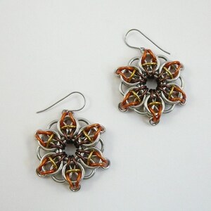 May include: A pair of handmade flower-shaped earrings. The earrings are made of silver-colored metal rings, with accents of copper and gold-colored metal. The earrings have a hook closure.