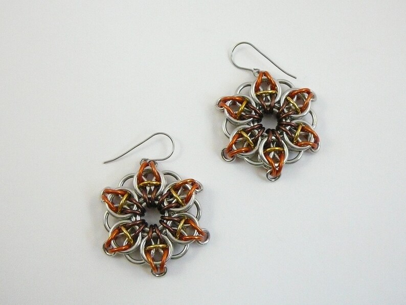 May include: A pair of handmade flower-shaped earrings. The earrings are made of silver-colored metal rings, with accents of copper and gold-colored metal. The earrings have a hook closure.