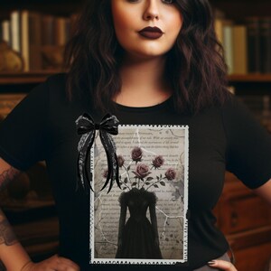 K&ouml;nnte beinhalten: Ein schwarzes T-Shirt mit einem Vintage-Bild einer Frau in einem schwarzen Kleid, aus dessen Kopf Rosen wachsen. Das Bild ist von einem wei&szlig;en Rahmen und einem schwarzen Band umgeben.