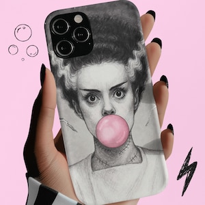 Peut inclure: Une coque de téléphone avec un croquis au crayon d'une femme aux cheveux foncés et une bulle de chewing-gum rose. Le cou de la femme est dessiné avec des points de suture. L'étui est gris et blanc avec un objectif d'appareil photo noir.
