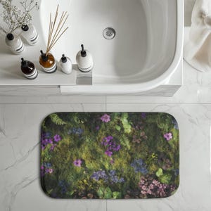 May include: A rectangular bath mat featuring a vibrant floral design with purple, blue, and pink flowers, green ferns, and moss. The mat is placed on a white tile floor near a white bathtub, creating a nature-inspired bathroom decor.