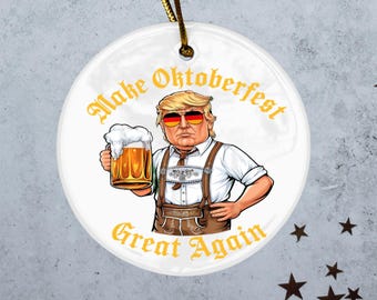 May include: White ceramic ornament featuring a cartoon illustration of a person in sunglasses and German attire, holding a beer stein. The text "Make Oktoberfest Great Again" is in gold lettering.