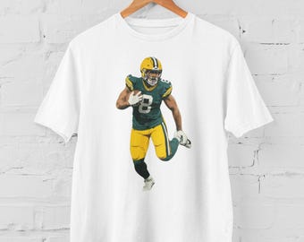 Peut inclure: T-shirt blanc avec un motif de joueur de football vert et jaune. Le joueur porte un casque et tient un ballon de football.