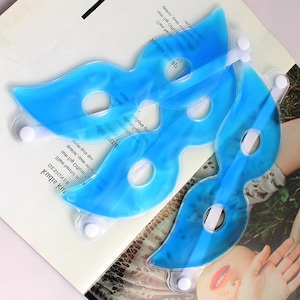 May include: Three blue gel eye masks with white elastic straps and button closures are arranged on a printed surface. The masks are in the shape of a butterfly or a stylized eye mask.