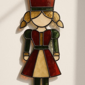 May include: Stained glass figure of a girl in a red and green dress, with a matching hat. The figure has blonde pigtails and is outlined in black. The glass is a mix of red, green, yellow, and cream colors.