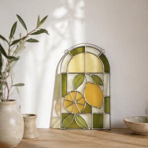 May include: Stained glass window panel featuring a lemon design. The panel has a curved top and is divided into sections of yellow, green, and white glass. The lemon design includes a whole lemon and a sliced lemon with green leaves.