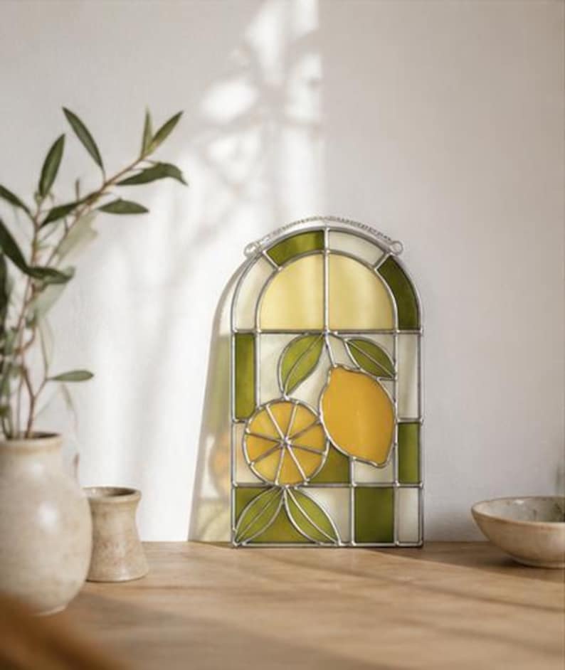 May include: Stained glass window panel featuring a lemon design. The panel has a curved top and is divided into sections of yellow, green, and white glass. The lemon design includes a whole lemon and a sliced lemon with green leaves.