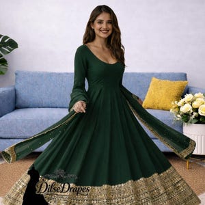 Puede incluir: Un vestido largo verde oscuro con una falda fluida y mangas largas. El vestido presenta detalles de lentejuelas doradas a lo largo del dobladillo y las mangas. El texto "Dilse Drapes" es visible en el vestido.