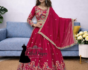 May include: A magenta-colored ethnic wear ensemble featuring a long-sleeved top and a flowing skirt, both adorned with intricate floral embroidery in various colors. A matching scarf is draped over the shoulder. The outfit is from Dilse Drapes.