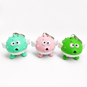 May include: Three colorful pufferfish keychains in green, pink, and green. Each keychain has a surprised expression, white wings, and small feet. The keychains are made of a soft material and have a metal keyring attached.