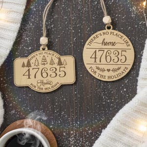 May include: Two wooden Christmas ornaments with the text "There's no place like home 47635 for the holidays". One is rectangular, the other is circular. The ornaments are hanging on twine.