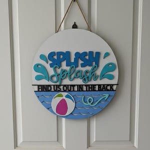 May include: Round wooden sign with the words "SPLISH Splash" in blue, with water splash graphics. The sign also says "FIND US OUT IN THE BACK" and features a beach ball graphic. A rope is used for hanging.