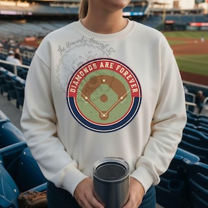Könnte beinhalten: Cremefarbenes Sweatshirt mit Baseball-Motiv. Die Grafik zeigt ein Baseballfeld-Design mit den Worten "Diamonds Are Forever" in einem kreisförmigen Rahmen. Das Sweatshirt hat lange Ärmel.