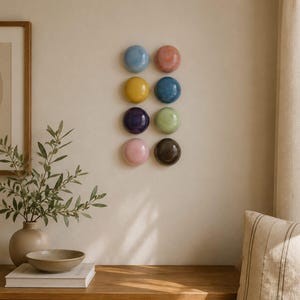 Puede incluir: Un conjunto de ocho objetos decorativos circulares, lisos y brillantes, montados en la pared y dispuestos en dos columnas verticales. Los colores incluyen azul claro, coral, amarillo, azul oscuro, morado, verde claro, rosa suave y marrón oscuro.