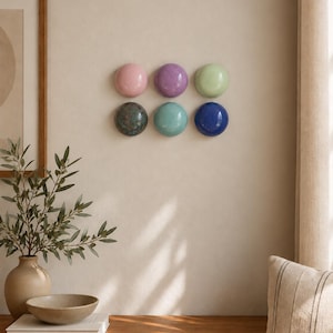 May include: A set of six circular, dome-shaped wall decorations arranged in two rows of three. The colours include light pink, purple, pale green, dark mottled grey, turquoise, and deep blue, each featuring a smooth, glossy, reflective finish.
