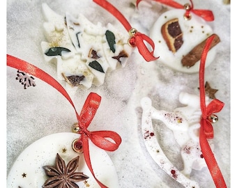 May include: A collection of white wax ornaments in shapes of Christmas trees, rocking horses, and circles. Each ornament is decorated with dried orange slices, star anise, pinecones, and gold glitter, finished with a bright red ribbon for hanging.