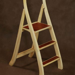 May include: A wooden step stool with a curved handle and three steps. The steps and seat are a reddish-brown color, contrasting with the light-colored wood frame. The stool is designed for reaching higher places.