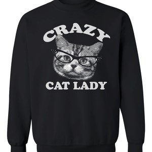 Könnte beinhalten: Schwarzes Sweatshirt mit dem weißen Schriftzug "CRAZY CAT LADY", der ein Halbtonbild einer Katze mit Brille einrahmt. Das Gesicht der Katze ist mit einem gepunkteten Muster versehen.