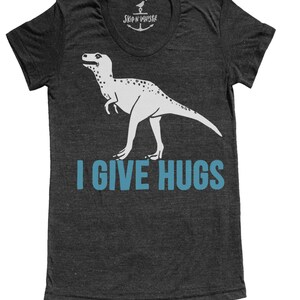 May include: Dark gray t-shirt with a white dinosaur graphic and the text "I GIVE HUGS" in blue. The shirt has a scoop neck and short sleeves. The brand name "SKIP N' WHISTLE" is printed at the neckline.
