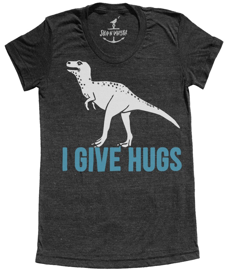 May include: Dark gray t-shirt with a white dinosaur graphic and the text "I GIVE HUGS" in blue. The shirt has a scoop neck and short sleeves. The brand name "SKIP N' WHISTLE" is printed at the neckline.