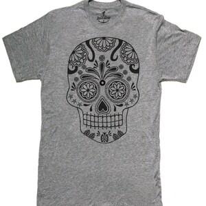 May include: A gray t-shirt featuring a detailed black sugar skull design. The skull has floral and star patterns, with the brand logo visible at the neckline. The shirt is made of a soft material.