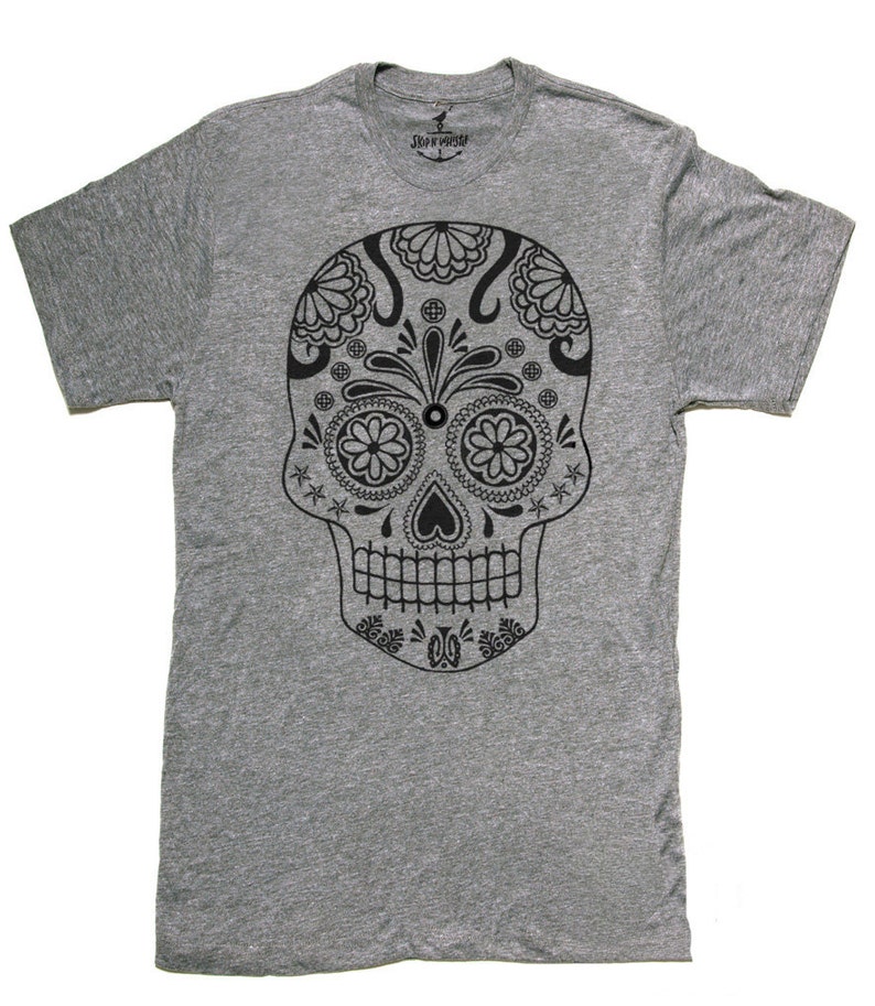 May include: A gray t-shirt featuring a detailed black sugar skull design. The skull has floral and star patterns, with the brand logo visible at the neckline. The shirt is made of a soft material.