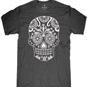 May include: Dark gray t-shirt featuring a detailed white sugar skull design. The skull has floral and geometric patterns, with a heart-shaped nose and a row of teeth. The shirt has a crew neck and short sleeves. The brand name "SKIN VAMPIRE" is printed on the neck.