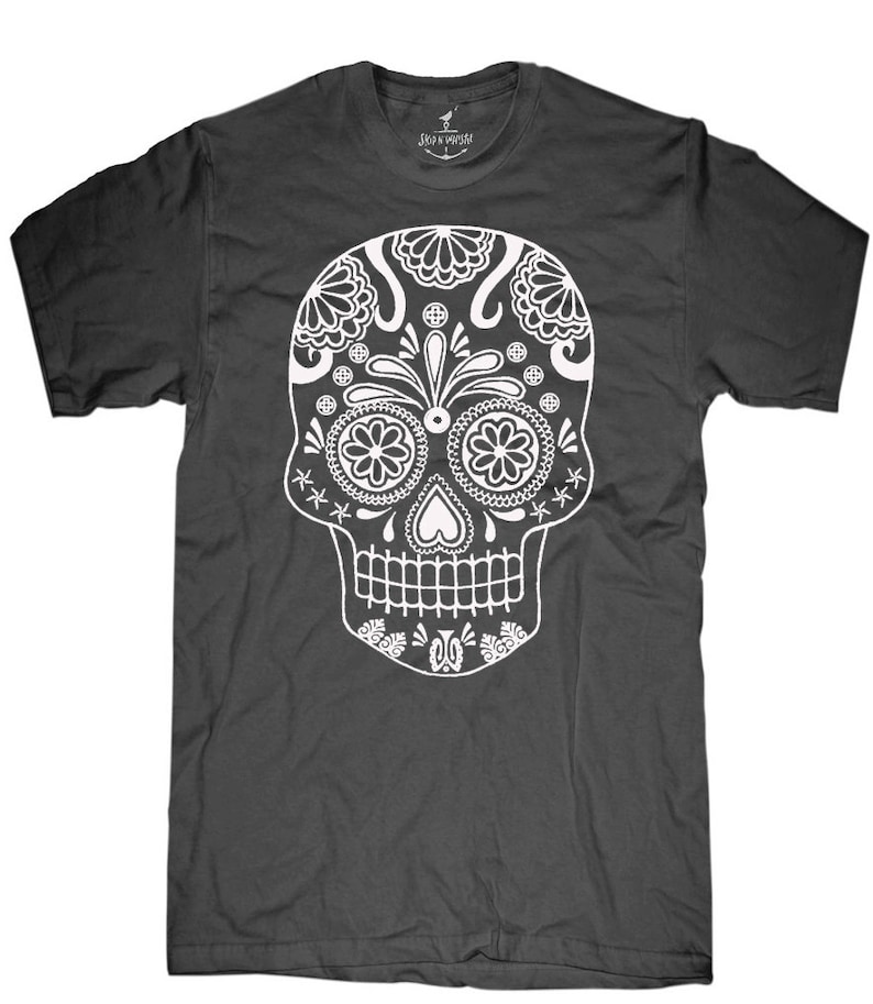 May include: Dark gray t-shirt featuring a detailed white sugar skull design. The skull has floral and geometric patterns, with a heart-shaped nose and a row of teeth. The shirt has a crew neck and short sleeves. The brand name "SKIN VAMPIRE" is printed on the neck.