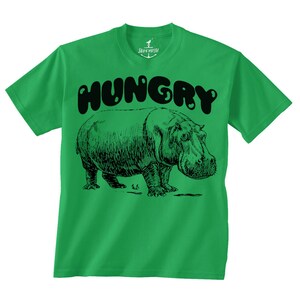 May include: Green t-shirt with a black graphic of a hippo and the word "HUNGRY" above it. The hippo is drawn in a detailed, vintage style. The shirt has a crew neck and short sleeves.
