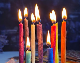 May include: A close-up shot of lit candles in various colors, including red, purple, yellow, and orange. The flames are bright and the candles are arranged closely together. The background is dark and out of focus.