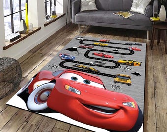 May include: A red cartoon race car with a smiling face is the focal point of this rug. The car is on a gray background with a black race track and other cartoon cars.