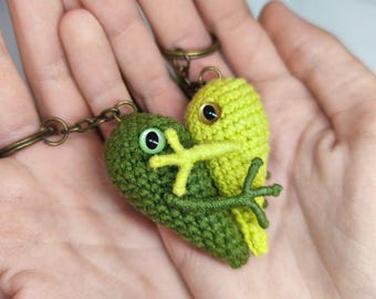 May include: A green and yellow crocheted frog keychain with a heart shape. The frogs are holding each other and have black eyes.