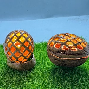 Op de afbeelding: Twee decoratieve, bolvormige kandelaars met een rasterontwerp. De kandelaars zijn bruin met een oranje gloed. Ze staan op groen gras. Elke kandelaar heeft een diameter van ongeveer 10 cm.