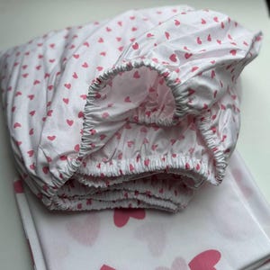 Op de afbeelding: Een wit hoeslaken met een roze hartjespatroon. Het laken is gevouwen en opgerold.