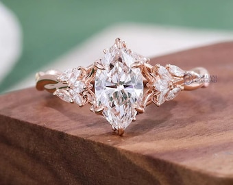 May include: A rose gold ring featuring a large marquise-cut center stone flanked by smaller marquise-cut stones arranged in a leaf-like pattern on each side. The band has a polished finish and the text Brillani Diamond is visible on the side.