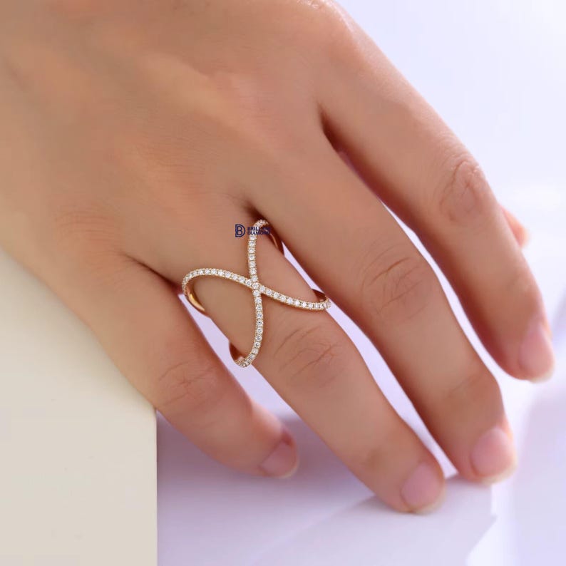 Puede incluir: Un anillo dorado con un dise&ntilde;o en forma de cruz, adornado con peque&ntilde;as piedras preciosas brillantes. El anillo se lleva en un dedo, mostrando su estilo elegante y moderno. Las piedras preciosas est&aacute;n engastadas en una l&iacute;nea continua, creando un efecto deslumbrante.