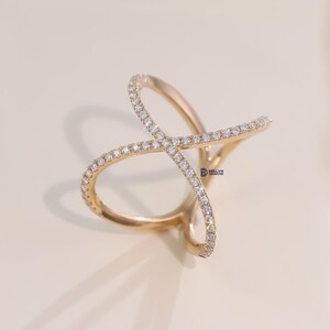 Puede incluir: Un anillo dorado con un dise&ntilde;o &uacute;nico e entrelazado. El anillo est&aacute; adornado con numerosos diamantes peque&ntilde;os y brillantes, creando una exhibici&oacute;n brillante. El dise&ntilde;o del anillo presenta dos bandas cruzadas, cada una bordeada con los peque&ntilde;os diamantes.
