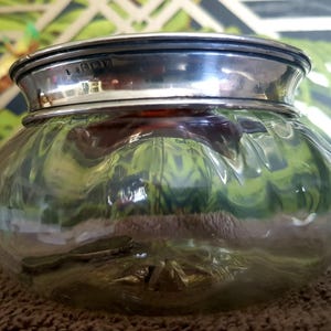 Könnte beinhalten: Ein klares Glasgefäß mit einem silbernen Deckel. Der Deckel trägt die Inschrift "K1001".