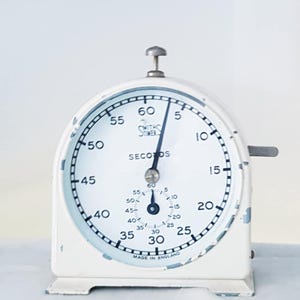 May include: A vintage white stopwatch with a black hand indicating the seconds. The face displays numbers from 5 to 60, with the text "SECONDS" and "MADE IN ENGLAND". The stopwatch has a silver winding knob.