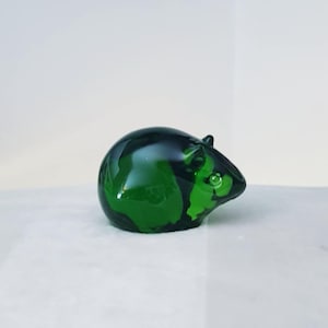 May include: A decorative glass mouse figurine in a deep green hue with darker green marbling. The mouse has small, rounded ears and a smooth, glossy finish. It is set against a white background. A charming ornament.