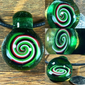 May include: A green glass pendant with a white, red, and black spiral design. The pendant is on a black cord.