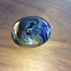 Puede incluir: Un mármol de vidrio colorido con remolinos de azul, verde, rojo y blanco.