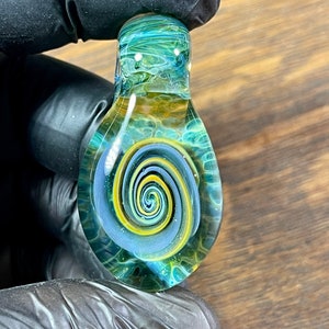May include: A glass pendant with a swirling blue, green, and yellow design. The pendant has a white spiral in the center.