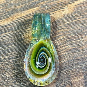 May include: A green and gold glass pendant with a spiral design. The pendant is made of dichroic glass, which means that it changes color depending on the angle of light.