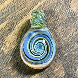 May include: A glass pendant with a swirling blue, white, and gold design. The pendant has a loop at the top for attaching to a chain.