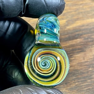 May include: A glass pendant with a swirling pattern of yellow, orange, blue, and green. The pendant has a clear glass top and a spiral design on the bottom.
