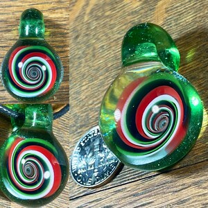 May include: A green glass pendant with a swirling red, white, and black design. The pendant has a hole at the top for a cord or chain.