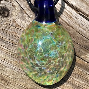 Peut inclure: Un pendentif en verre vert et bleu avec une bélière en verre bleu foncé. Le pendentif a un motif marbré tourbillonnant.