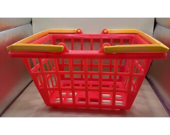 Op de afbeelding: Een felrode plastic winkelmand met een gele handgreep. De mand heeft een rechthoekige vorm met een rasterpatroon. De handgreep heeft een contrasterende gele kleur.
